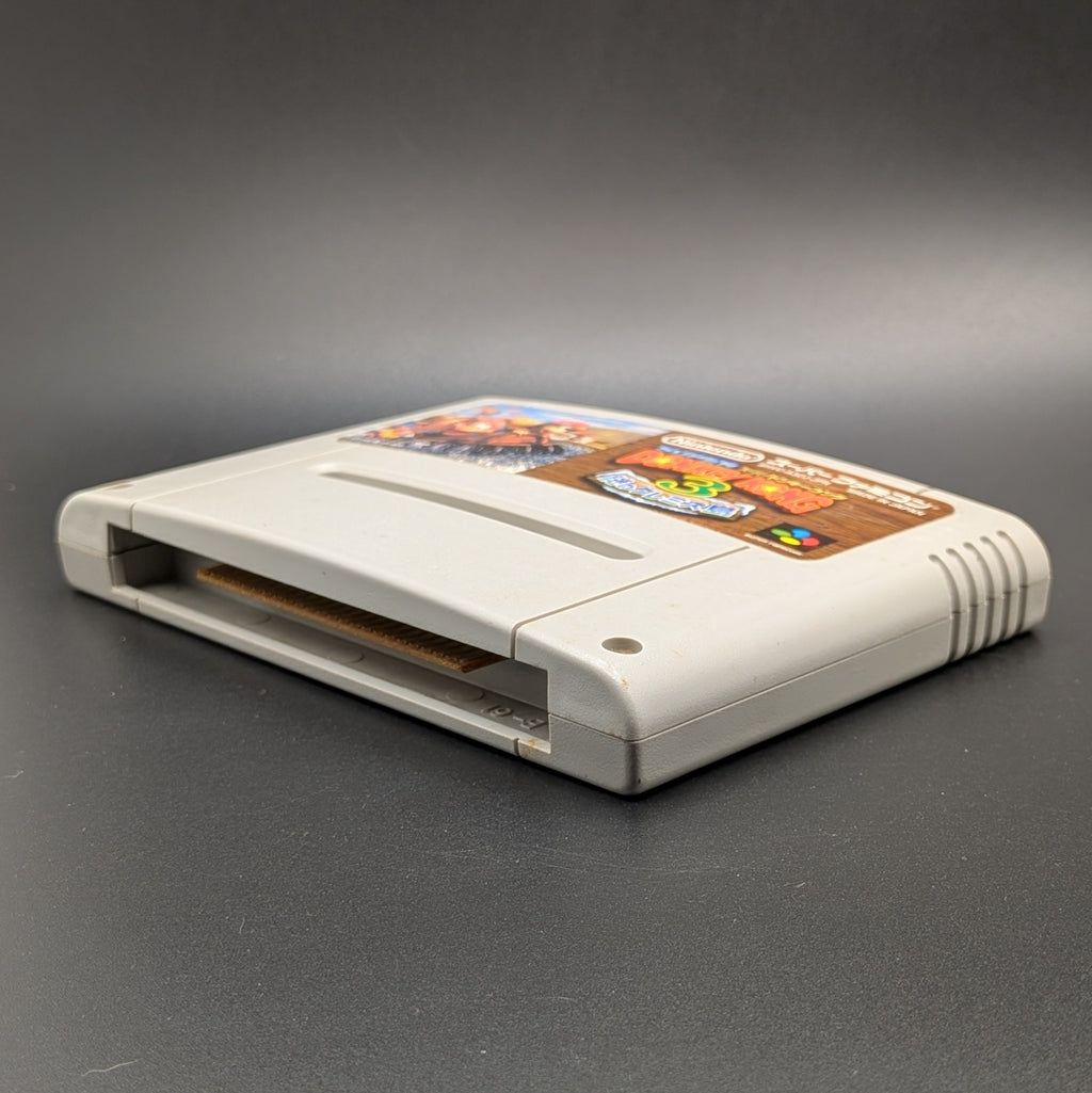 Super Donkey Kong 3 video game cartridge for Nintendo's Super Famicom (SFC) Entertainment System, shown laying on its back with the label facing up and the bottom slot is visible. Pictured on a dark grey background.
