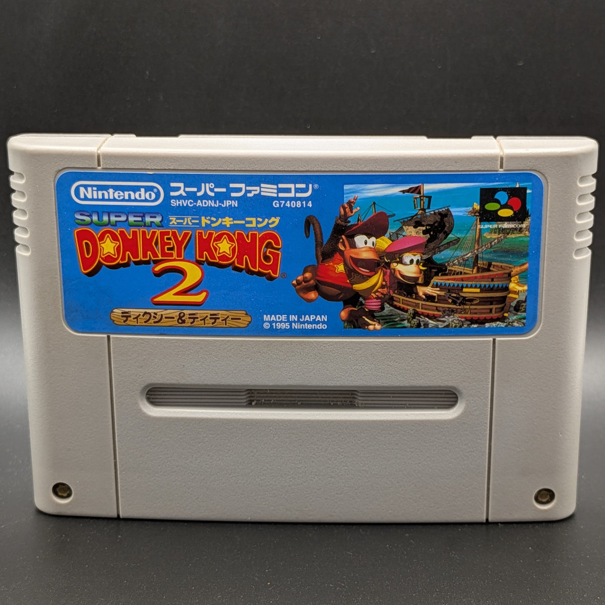 A close up of Donkey Kong 2 video game cartridge for Nintendo's Super Famicom (SFC) Entertainment System, shown standing up and facing forward on a dark grey background.
