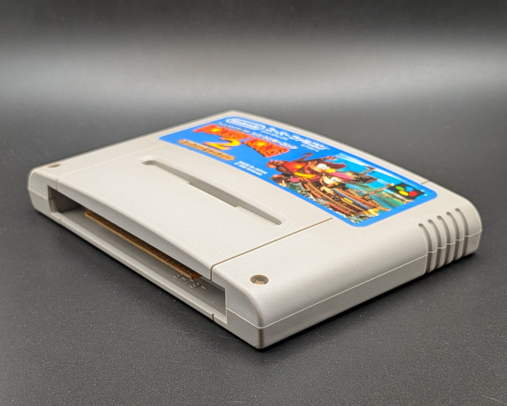 Donkey Kong 2 video game cartridge for Nintendo's Super Famicom (SFC) Entertainment System, shown laying on its back and facing up, on a dark grey background.
