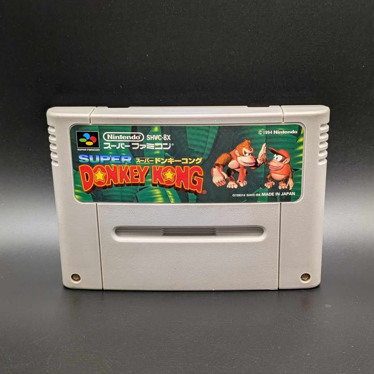 Super Donkey Kong video game cartridge for Nintendo's Super Famicom (SFC) Entertainment System, shown standing up and facing forward on a dark grey background.
