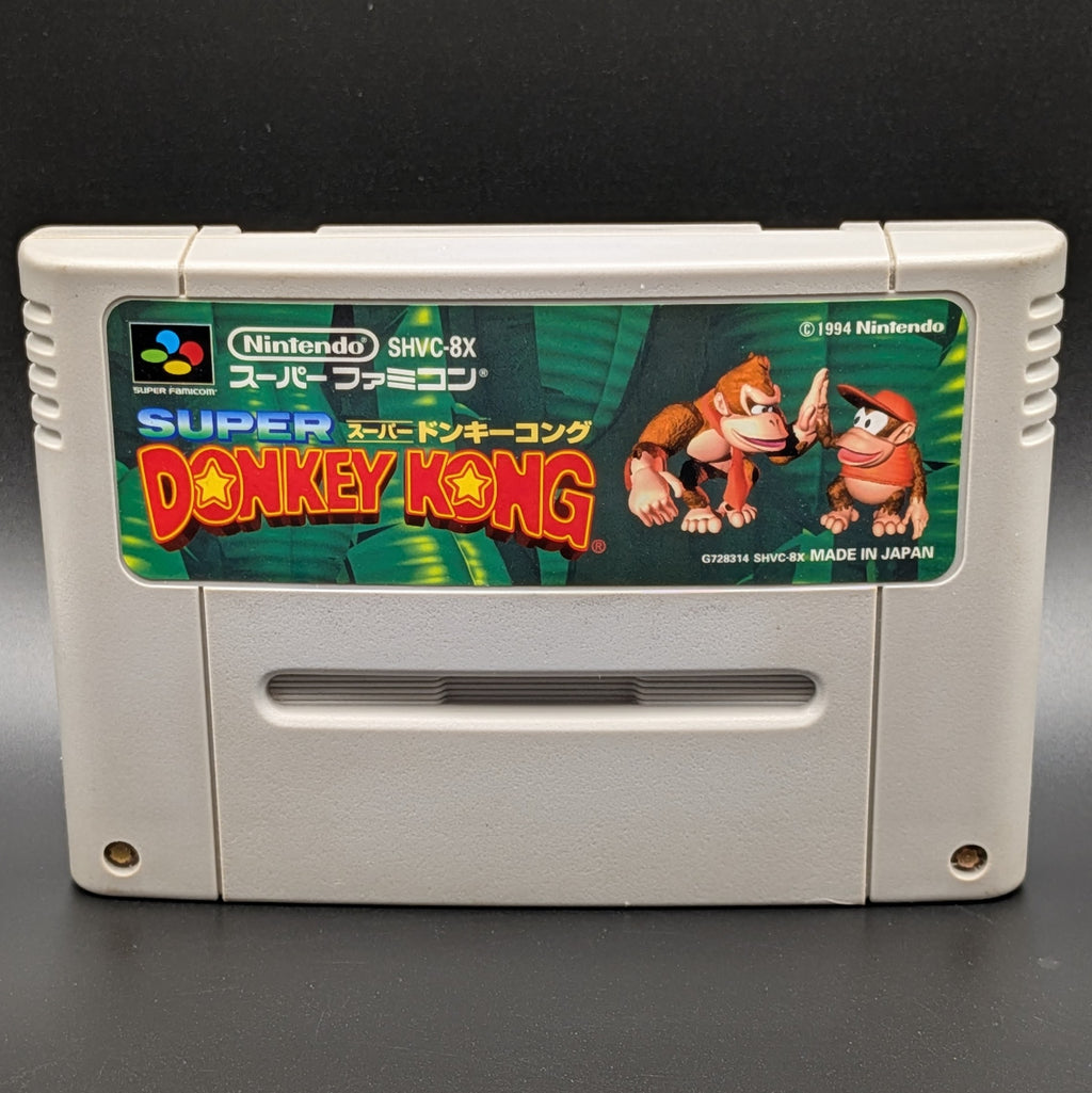 A close up of Super Donkey Kong video game cartridge for Nintendo's Super Famicom (SFC) Entertainment System, shown standing up and facing forward on a dark grey background.
