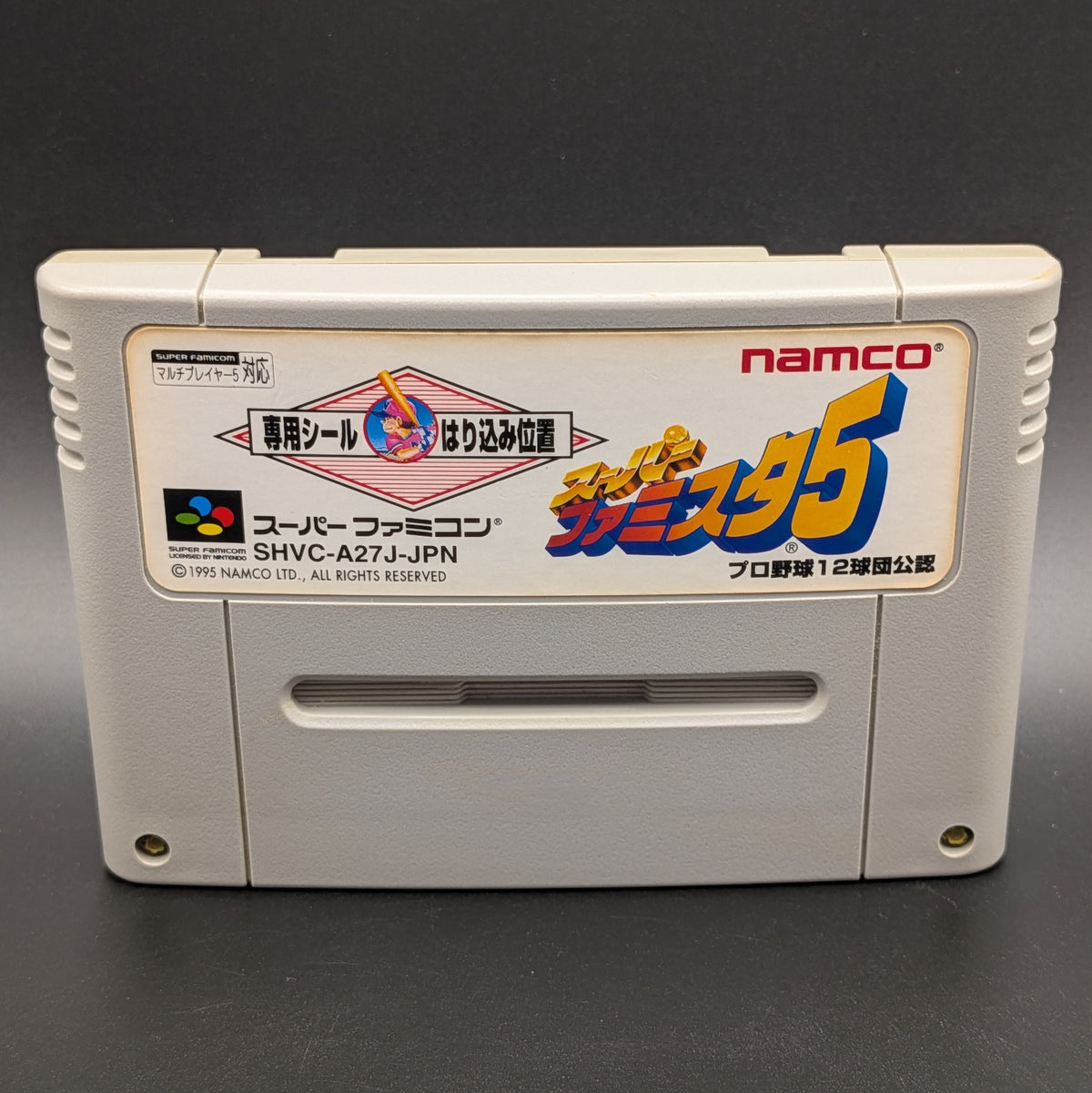 A close up of a Super Famista 5 video game cartridge for Nintendo's Super Famicom (SFC) Entertainment System, shown standing up and facing forward on a dark grey background.
