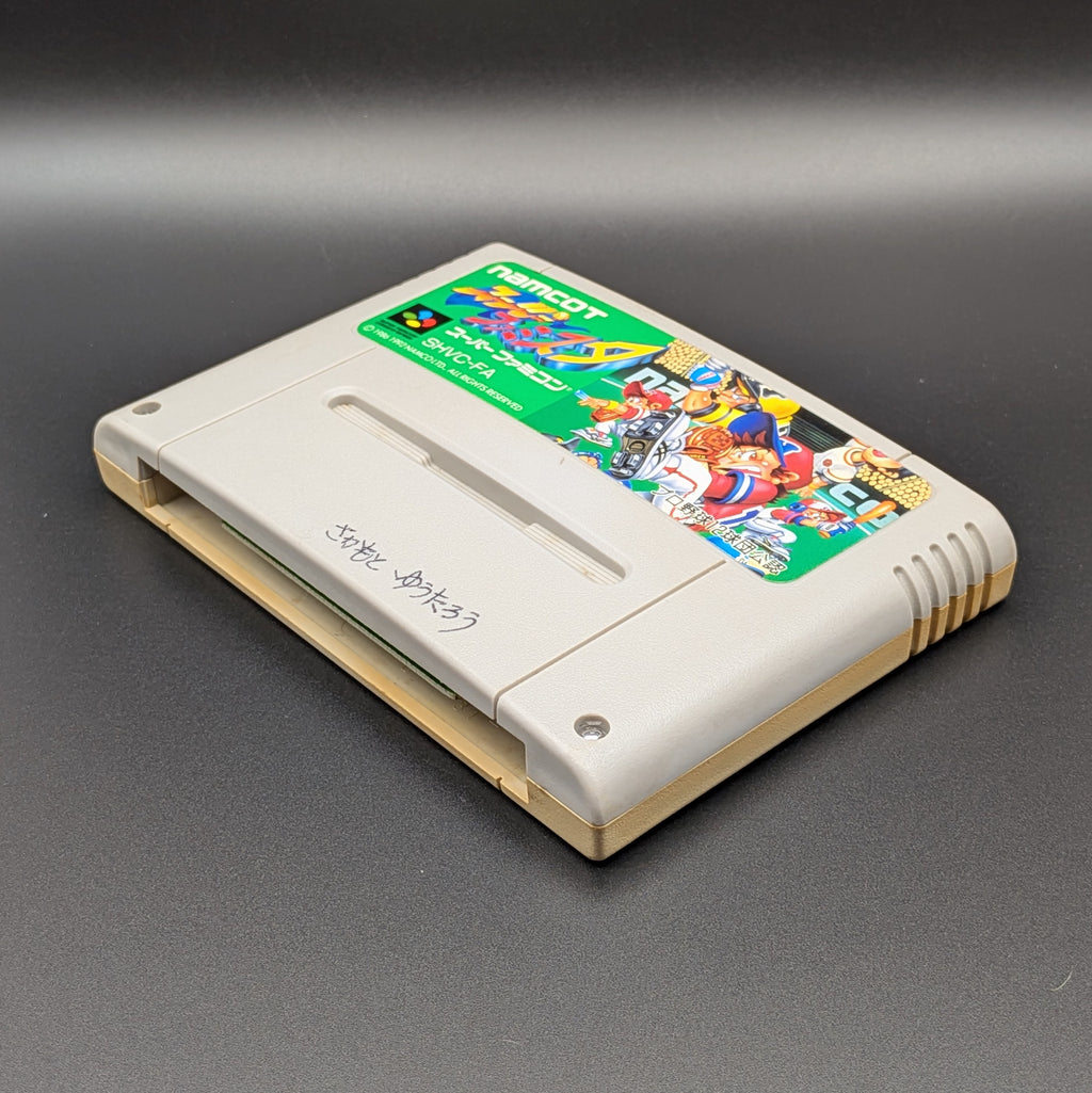 Super Famista video game cartridge for Nintendo's Super Famicom (SFC) Entertainment System, shown laying on its back with the label facing upwards. Showing the right hand side and bottom slot. It is displayed on a dark grey background.