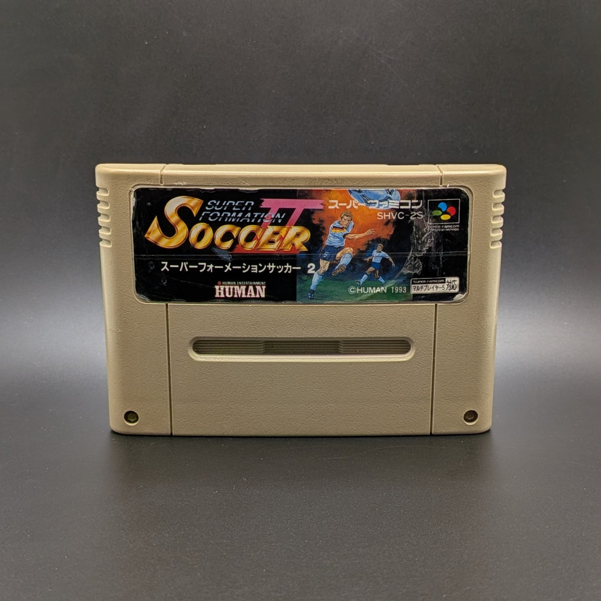 Super Formation Soccer 2 video game cartridge for Nintendo's Super Famicom (SFC) Entertainment System, shown standing up and facing forward on a dark grey background.
