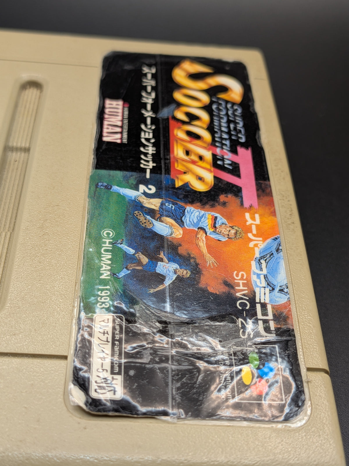 Super Formation Soccer 2 video game cartridge for Nintendo's Super Famicom (SFC) Entertainment System, showing a close up of the tapped label, on a dark grey background.
