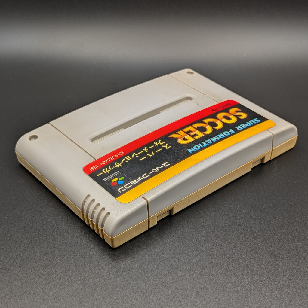 Super Formation Soccer video game cartridge for Nintendo's Super Famicom (SFC) Entertainment System, shown laying on its back with the label facing upwards. Showing the right hand side and top edge. It is displayed on a dark grey background.