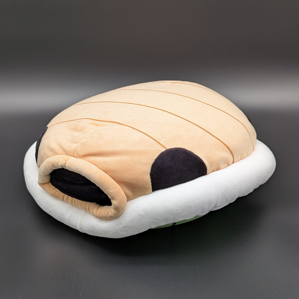 A green turtle shell plushie with a white padded rim, laying on its back to show the tan underside, and black accent details, photographed on a dark grey background. From Nintendo's beloved Super Mario and Mario Kart games,