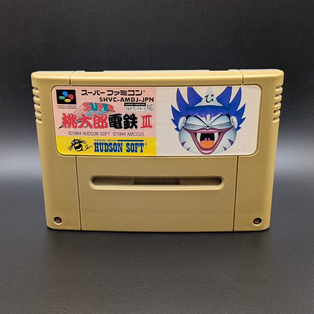 Super Momotarou Dentetsu 3 video game cartridge for Nintendo's Super Famicom (SFC) Entertainment System, shown standing up and facing forwards on a dark grey background.