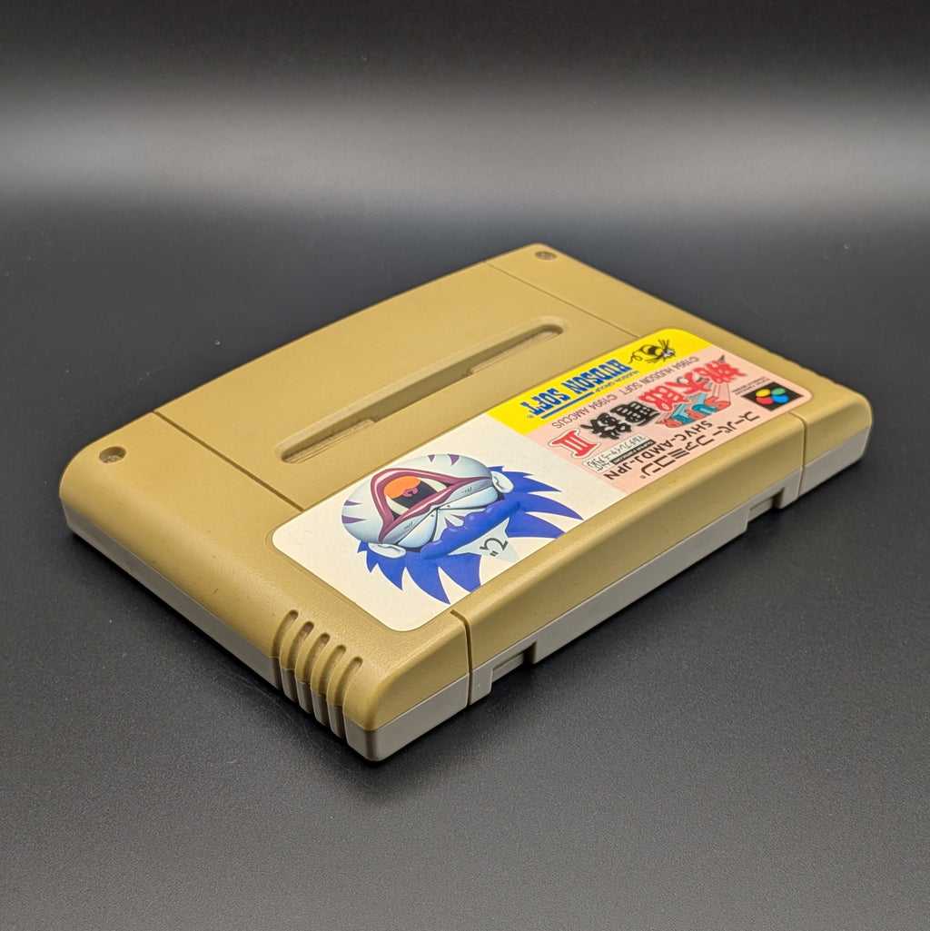 Super Momotarou Dentetsu 3 video game cartridge for Nintendo's Super Famicom (SFC) Entertainment System, shown laying on its back with the label facing upwards. Showing the right hand  and top edge. It sits on a dark grey background