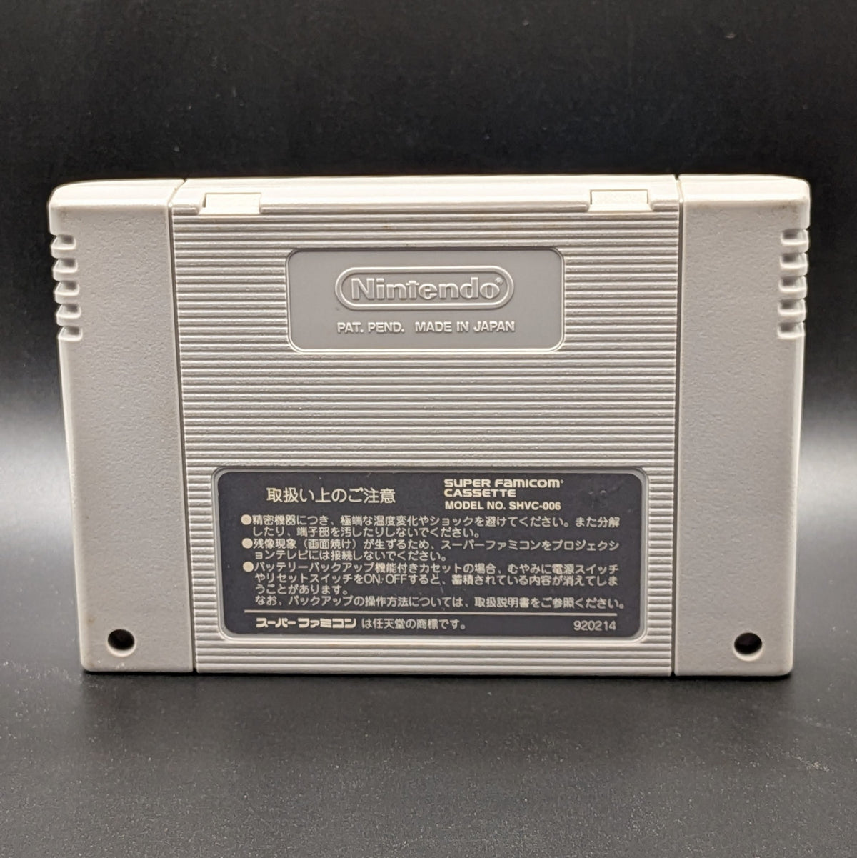 The image shows the back of the SFC cart, for the game Super Nazo Puyo Rulue no Roux for the  Super Famicom.  You can see the imprinted Nintendo logo and back label, which is in Japanese. Pictured on a black background. 
