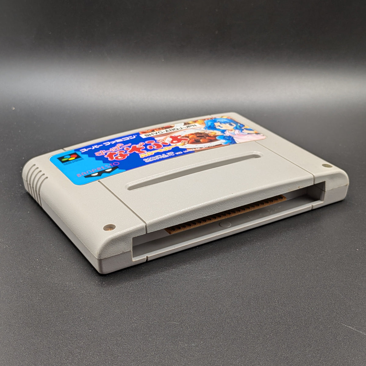 Super Nazo Puyo Rulue no Roux for the  Super Famicom. The SFC Cart is laying on its back, shown at a 3/4 angle to show the front and bottom of the cart. Pictured on a black background. 