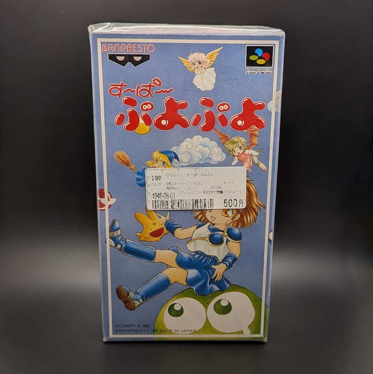 Super Puyo Puyo boxed and sealed video game cartridge for Nintendo's Super Famicom (SFC) Entertainment System, shown standing face on, on a dark grey background. There is a Japanese store sticker stuck to the front on the outer packaging.
