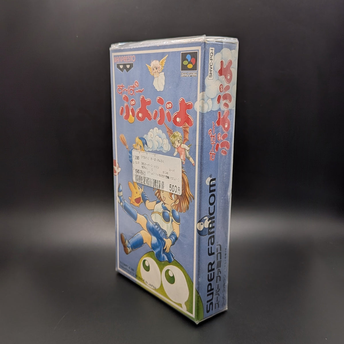 Super Puyo Puyo boxed and sealed video game cartridge for Nintendo's Super Famicom (SFC) Entertainment System, shown standing up at 3/4 angle facing the left, central on a dark grey background. There is a Japanese store sticker stuck to the front on the outer packaging.
