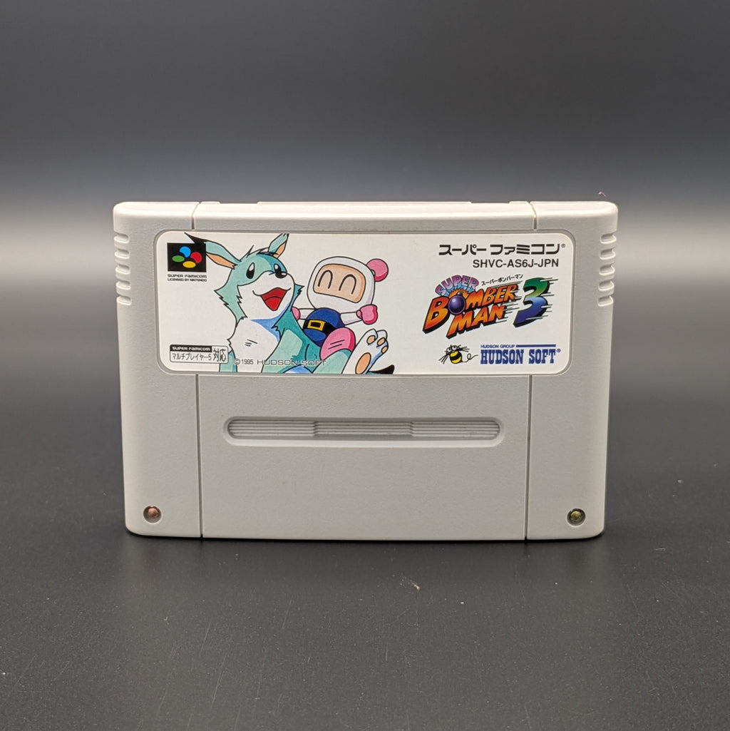 Super Bomberman 3 video game cartridge for Nintendo's Super Famicom (SFC) Entertainment System, shown standing up and facing forwards on a dark grey background.