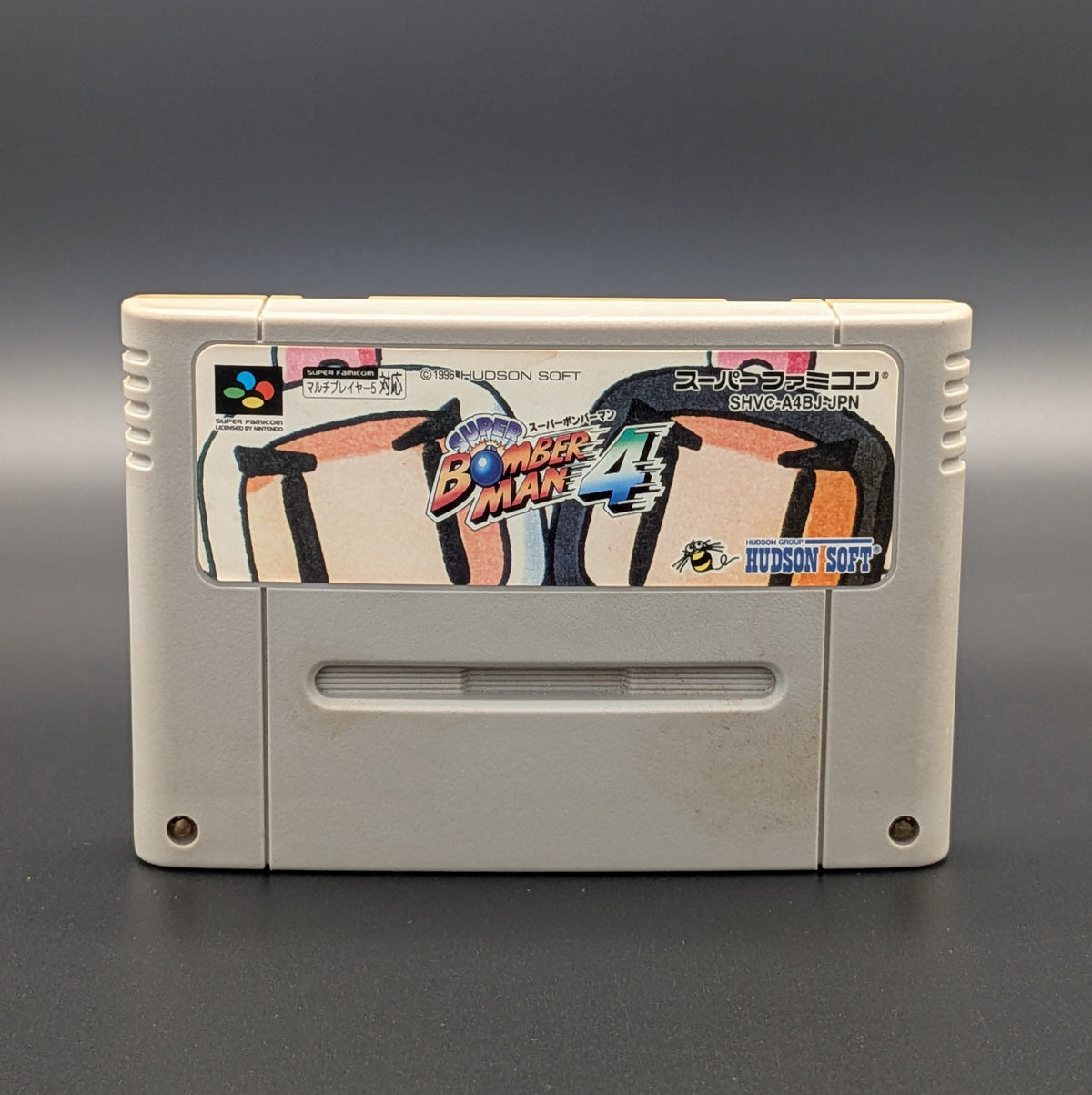 Super Bomberman 4 video game cartridge for Nintendo's Super Famicom (SFC) Entertainment System, shown standing up and facing forward on a dark grey background.
