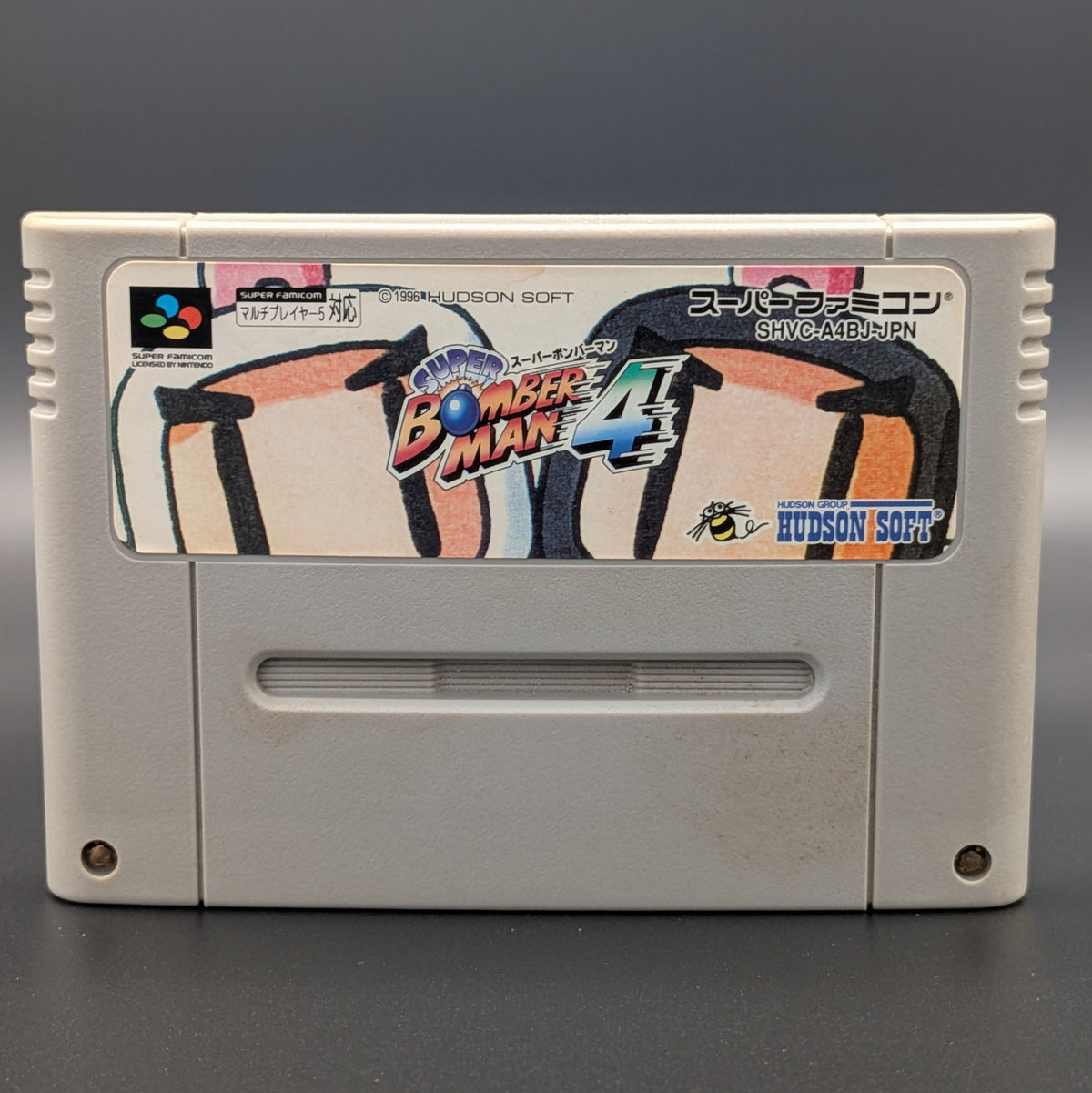 a close up of Super Bomberman 4 video game cartridge for Nintendo's Super Famicom (SFC) Entertainment System, shown standing up and facing forward on a dark grey background.
