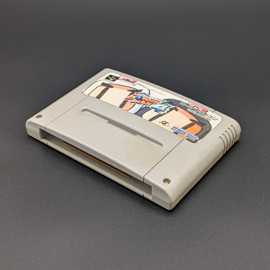 Super Bomberman 4 video game cartridge for Nintendo's Super Famicom (SFC) Entertainment System, shown laying on its back with the label facing upwards. It sits on a dark grey background.
