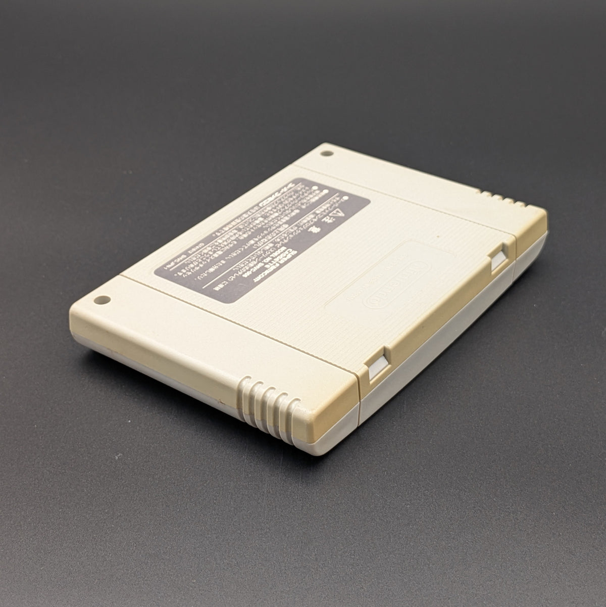 Super Bomberman 4 video game cartridge for Nintendo's Super Famicom (SFC) Entertainment System, shown laying on its back, showing the back label. It sits on a dark grey background.
