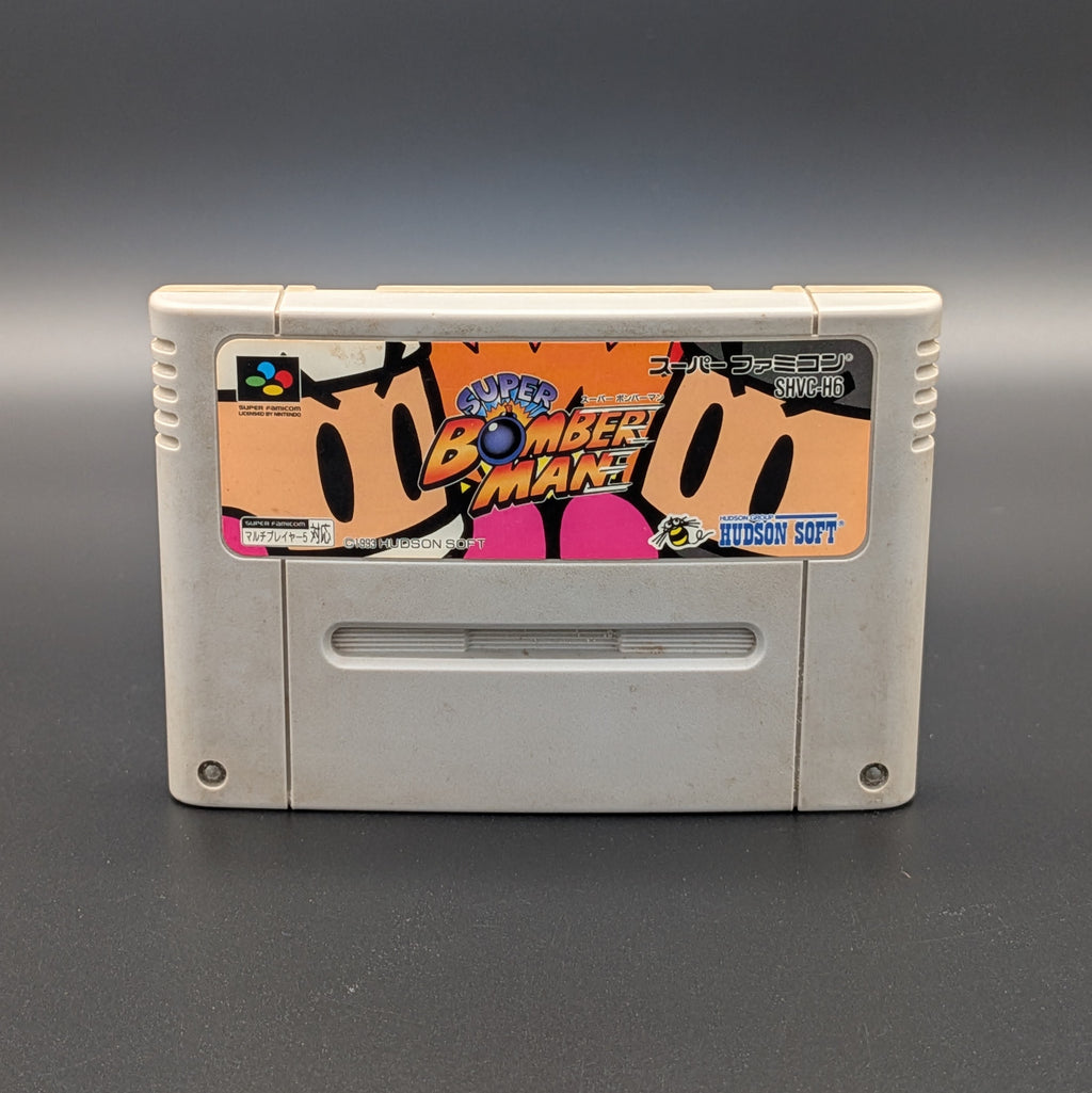 Super Bomberman video game cartridge for Nintendo's Super Famicom (SFC) Entertainment System, shown standing up and facing forwards on a dark grey background.