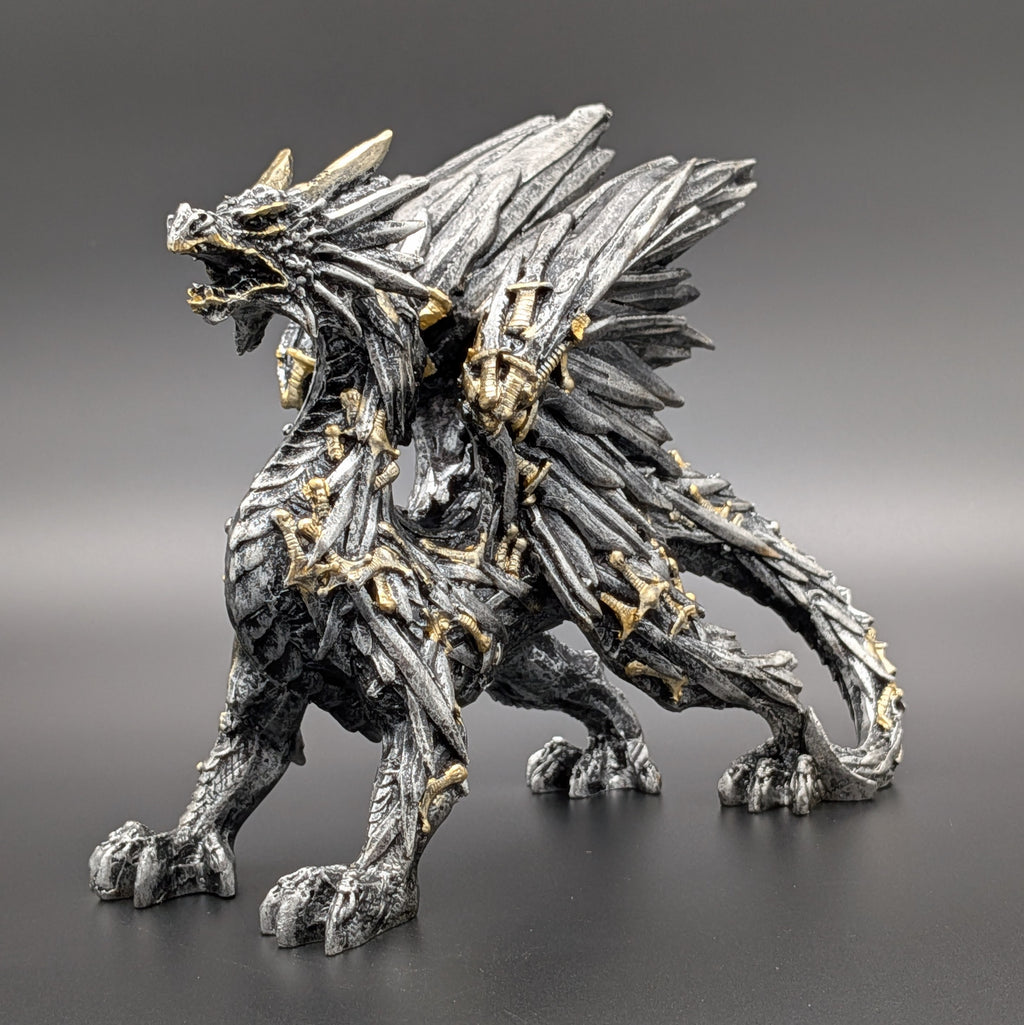 A detailed fantasy dragon figurine in a metallic silver-gray finish with gold accents, standing on a dark gray surface against a matching gray gradient background.
