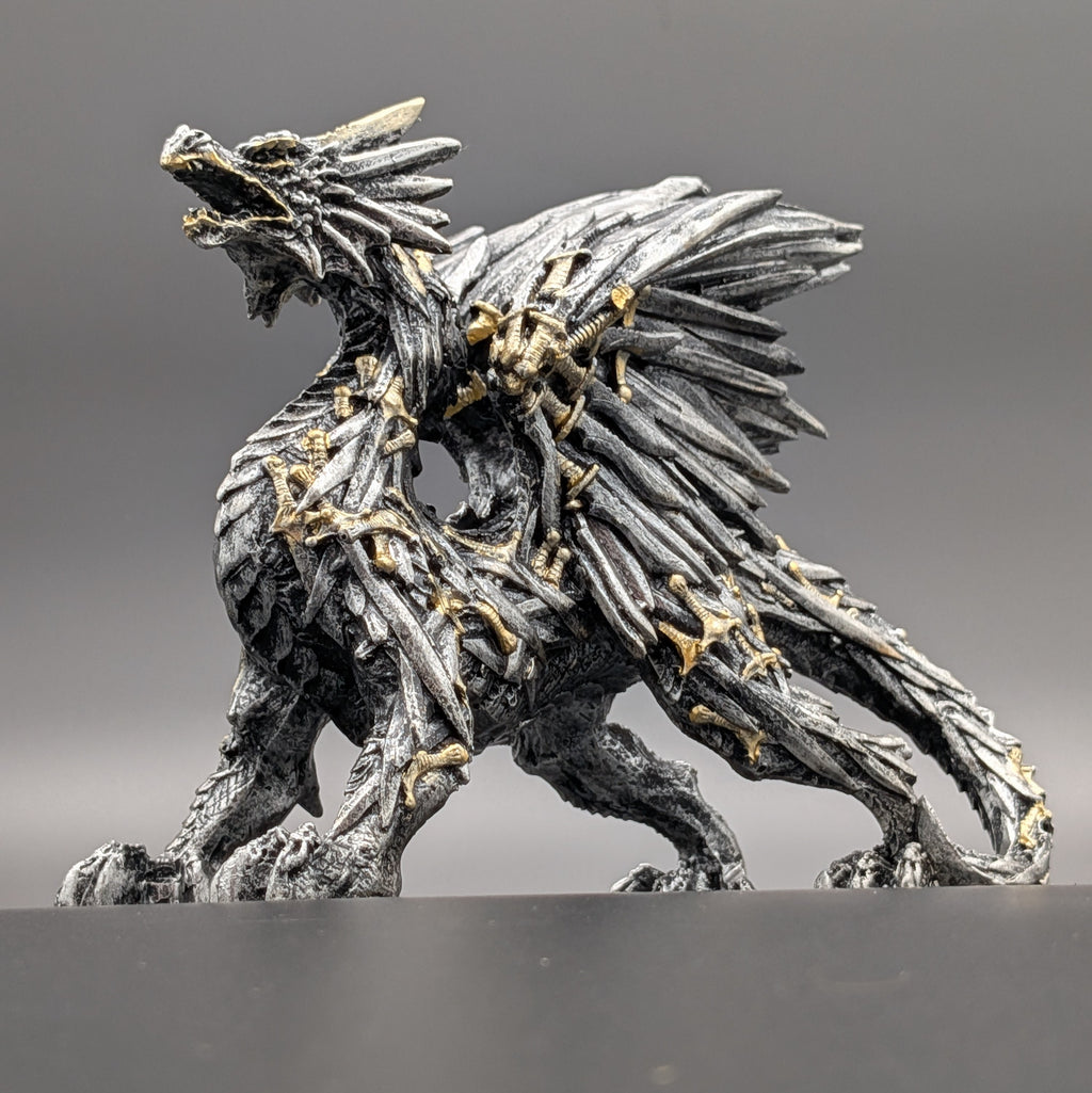 A detailed fantasy dragon figurine in a metallic silver-gray finish with intricate gold accents, shown against a neutral gray background.