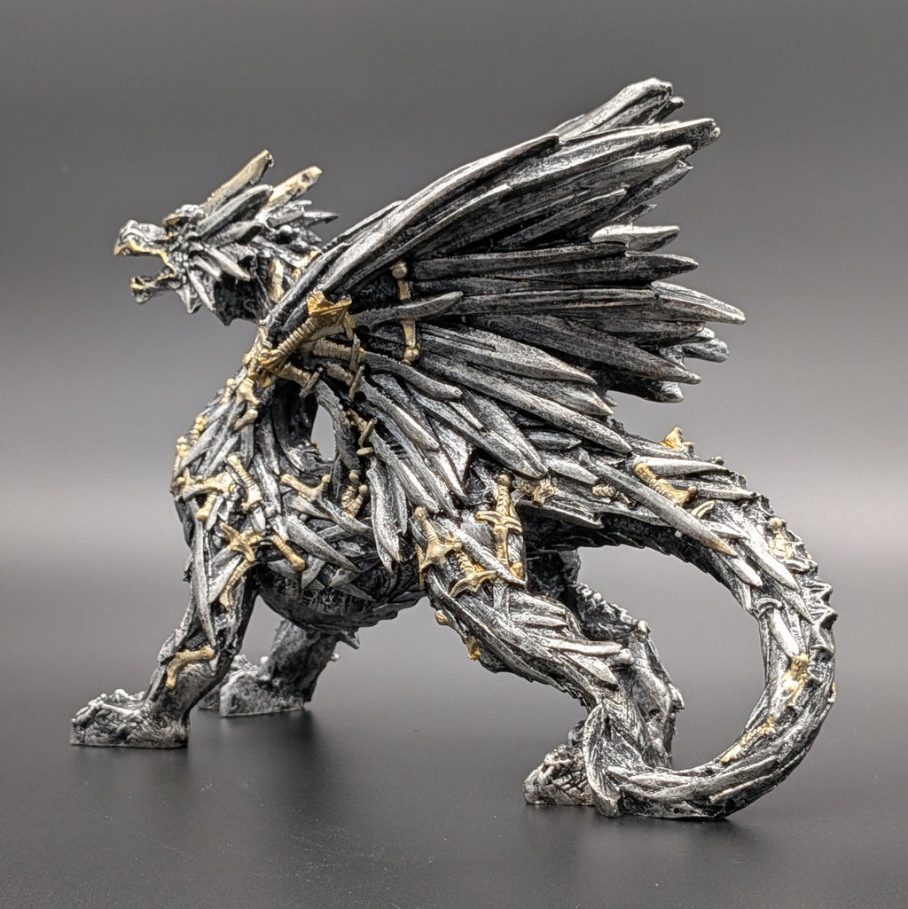 A detailed fantasy dragon figurine crafted from metallic silver swords with small gold accents, shown in a dynamic crouching pose against a dark gray gradient background.