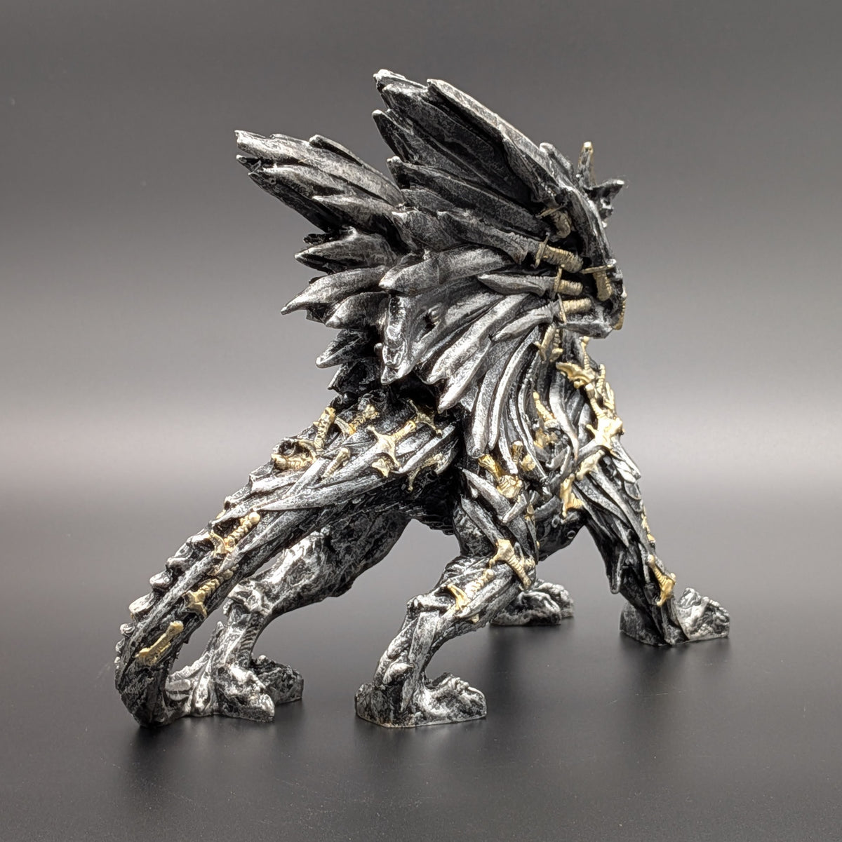 A detailed fantasy creature figurine with a textured, bark-like body, metallic silver-gray scales, and small gold accents, standing on a dark surface against a gray gradient background.