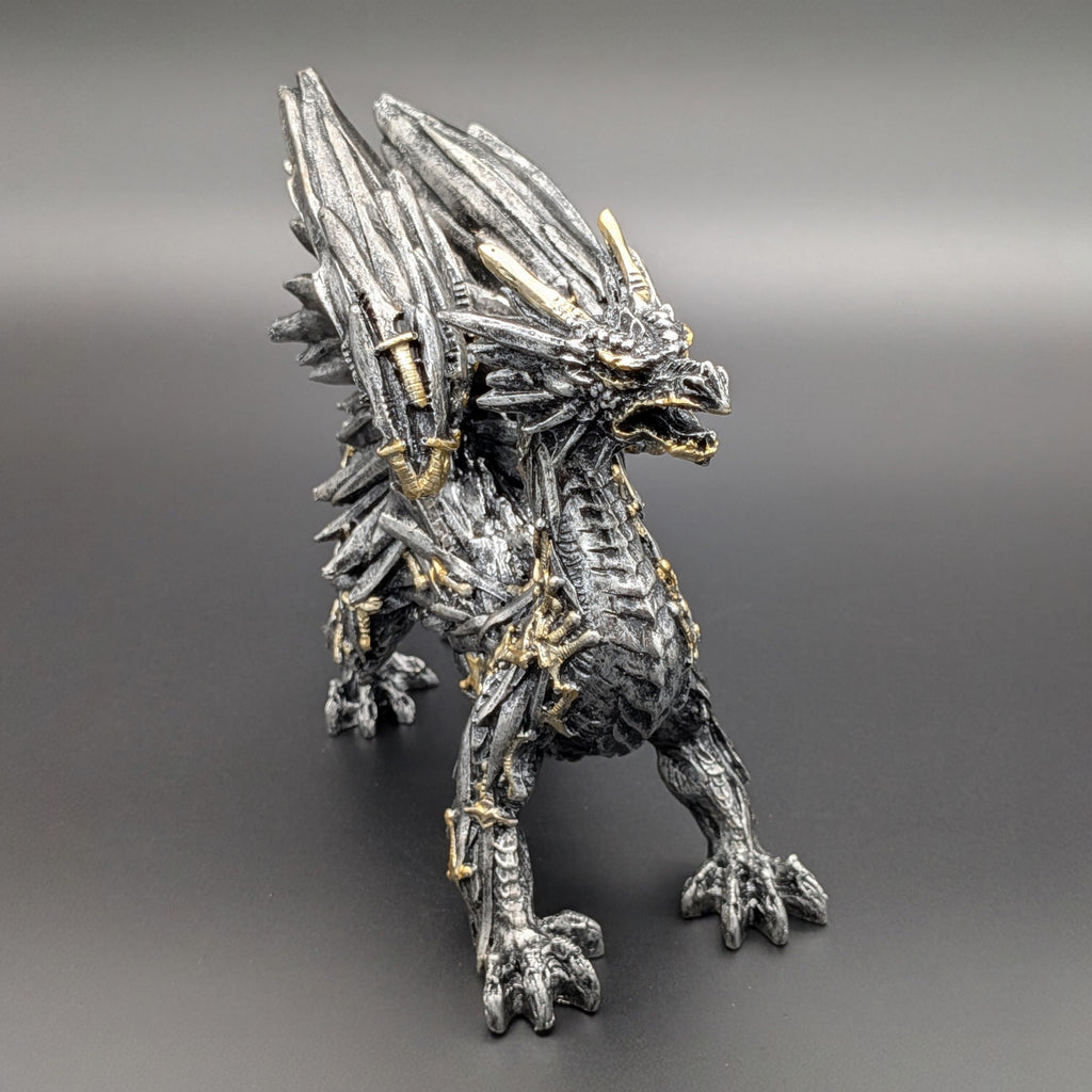 A detailed fantasy dragon figurine in a metallic silver and black textured finish with gold accents, standing on a dark gray gradient background.