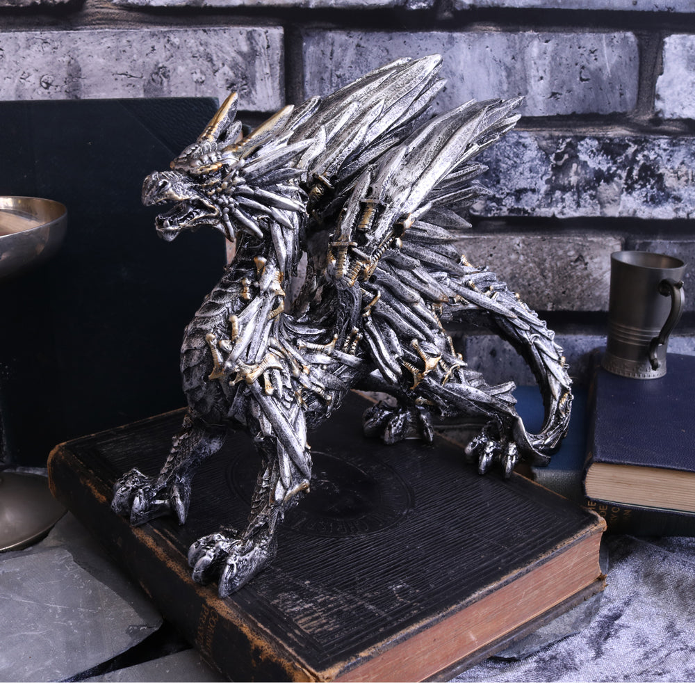 A metallic silver dragon figurine with gold accents, standing on an old book in a styled tabletop setting with a gray brick background.