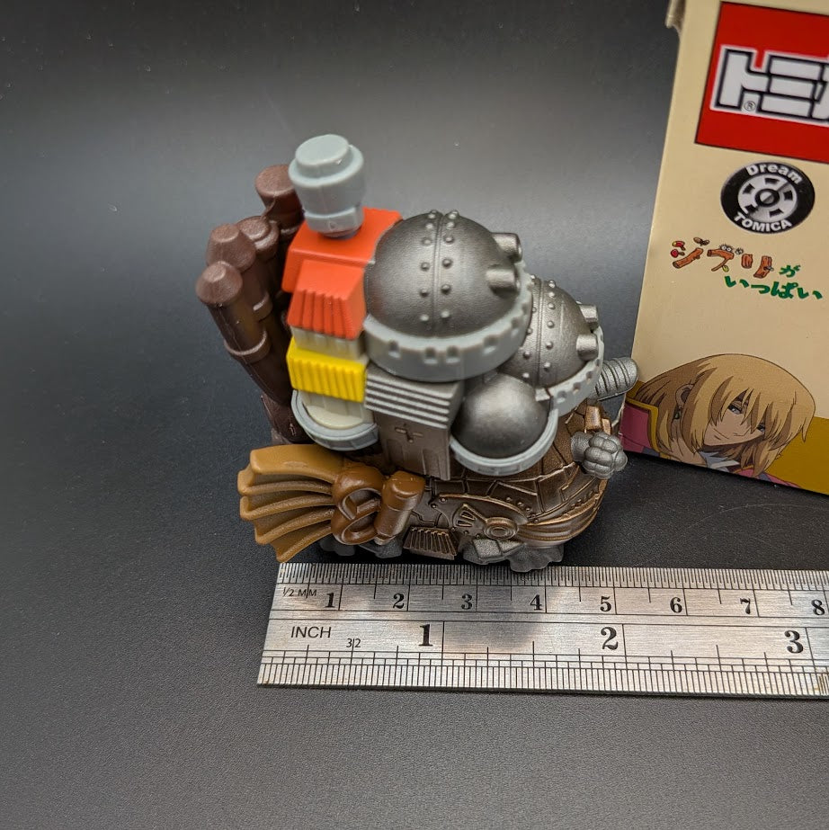 Howls Moving Castle Tomica Dream  Model No.8 - Side view of the model next to its box and a ruler for scale on a dark gray background.