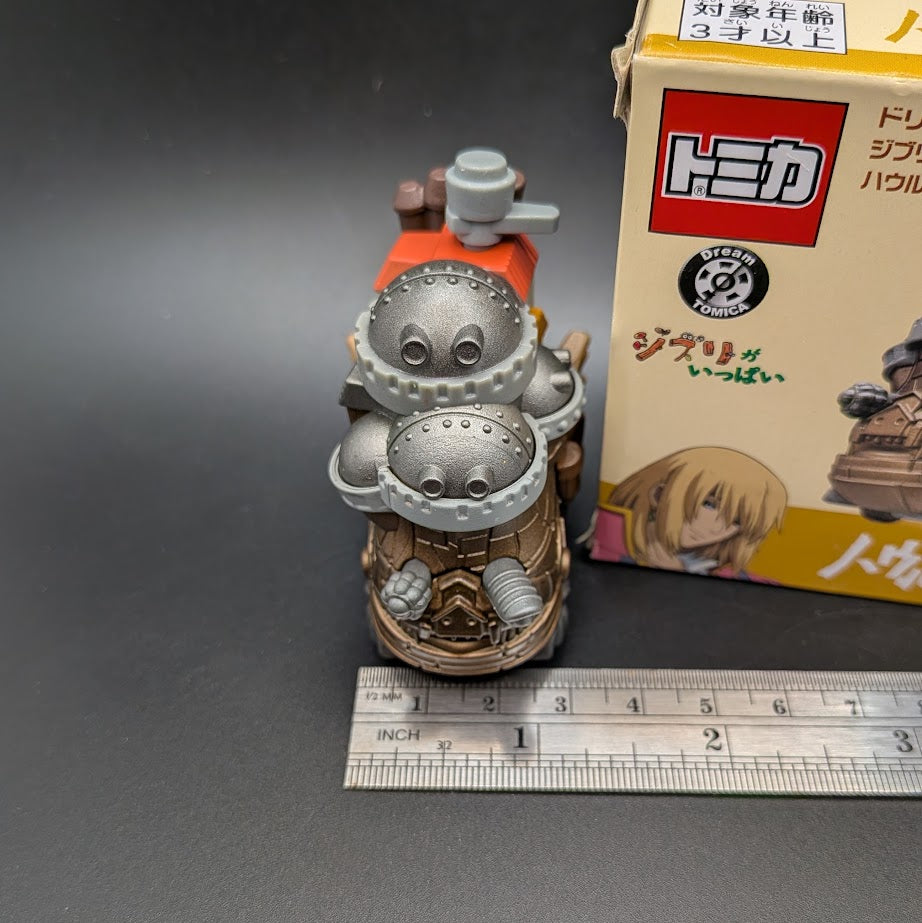 Howls Moving Castle Tomica Dream  Model No.8 - Front view of the model next to its box and a ruler for scale on a dark gray background.