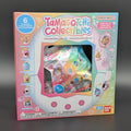 Tamagatchi Collectibles toy packaging box by Bandai Namco, featuring a colorful design with character illustrations and a clear window showing the packaged collectible inside, set against a dark gray background.