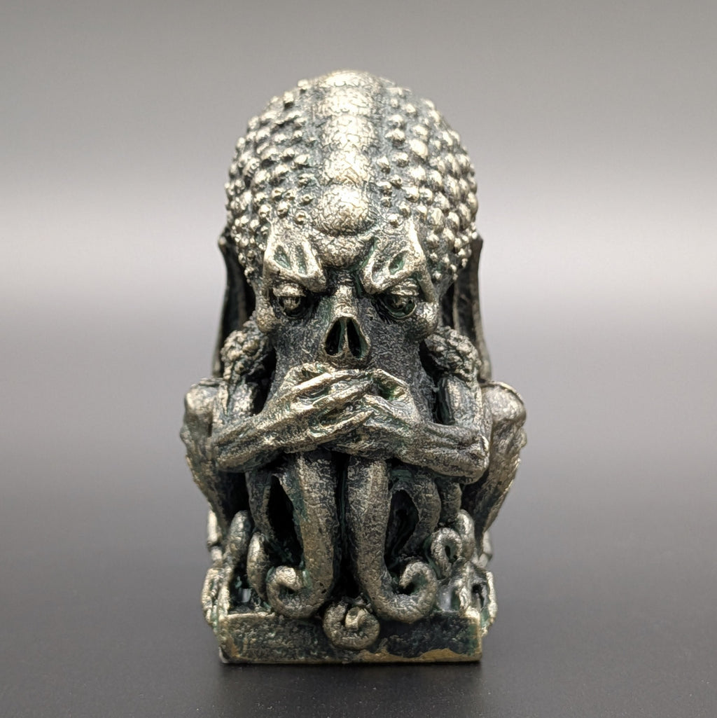 A polyresin Cthulhu figurine with a weathered stone patina & textured skin, depicting "Speak no evil" by covering his mouth, displayed on a dark grey background.