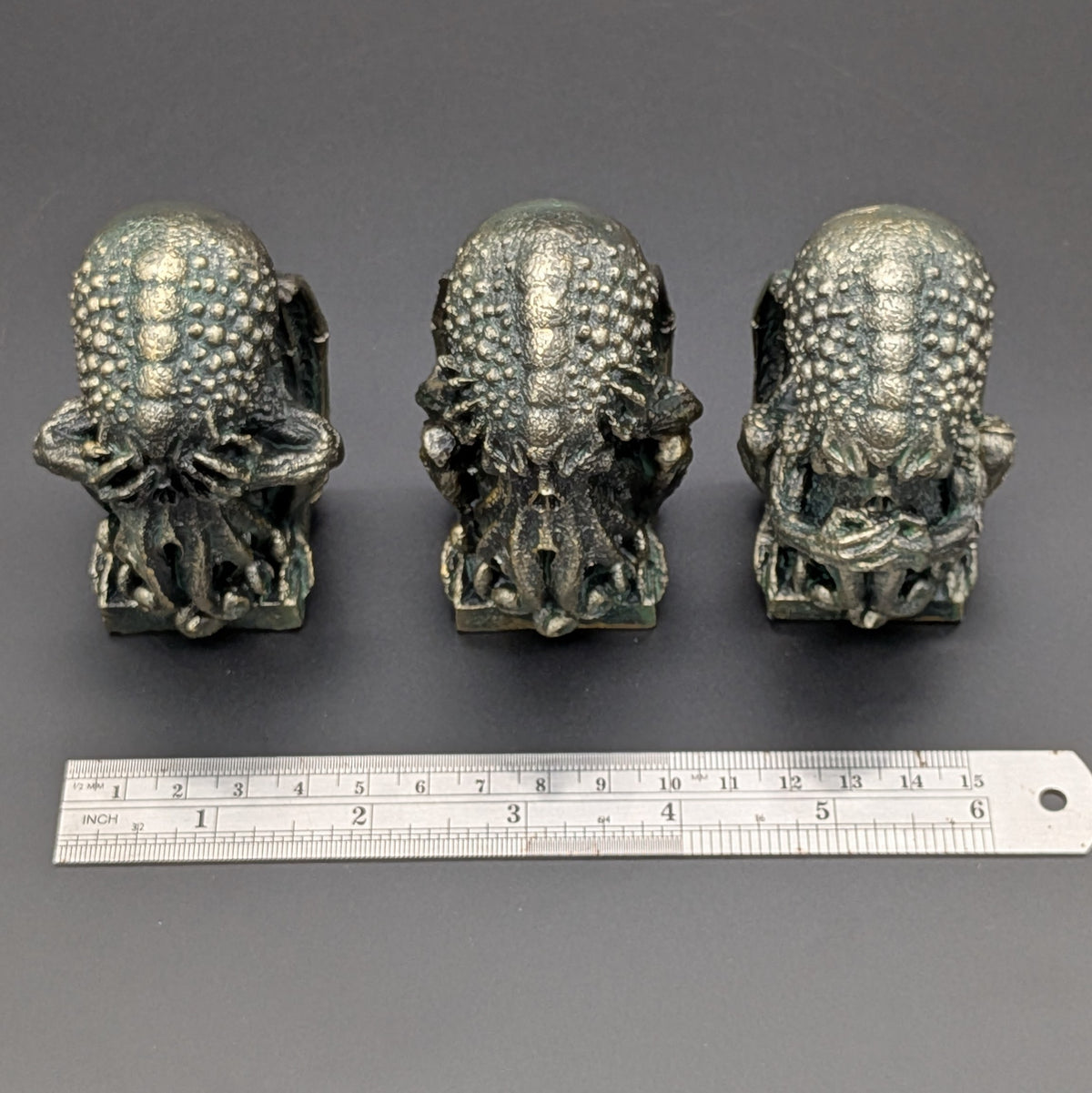 Three polyresin gothic-style Cthulhu shown side-by-side on a dark gray background, with a metal ruler below them for scale.