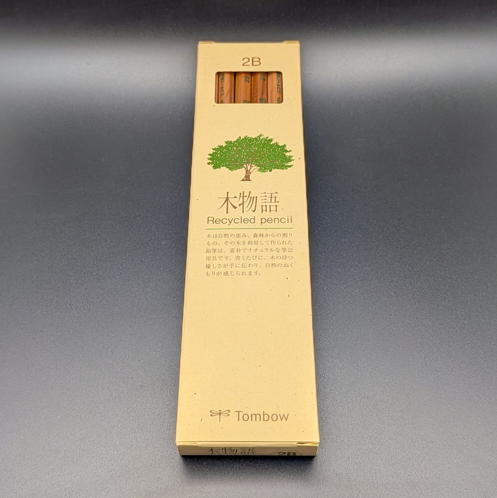 A tall, narrow beige cardboard box for Tombow 2B Recycled pencil, featuring a green tree illustration and Japanese text, set against a dark grey background.