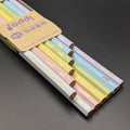 A set of pastel-colored wooden pencils with a tan paper label, photographed on a dark gray surface.