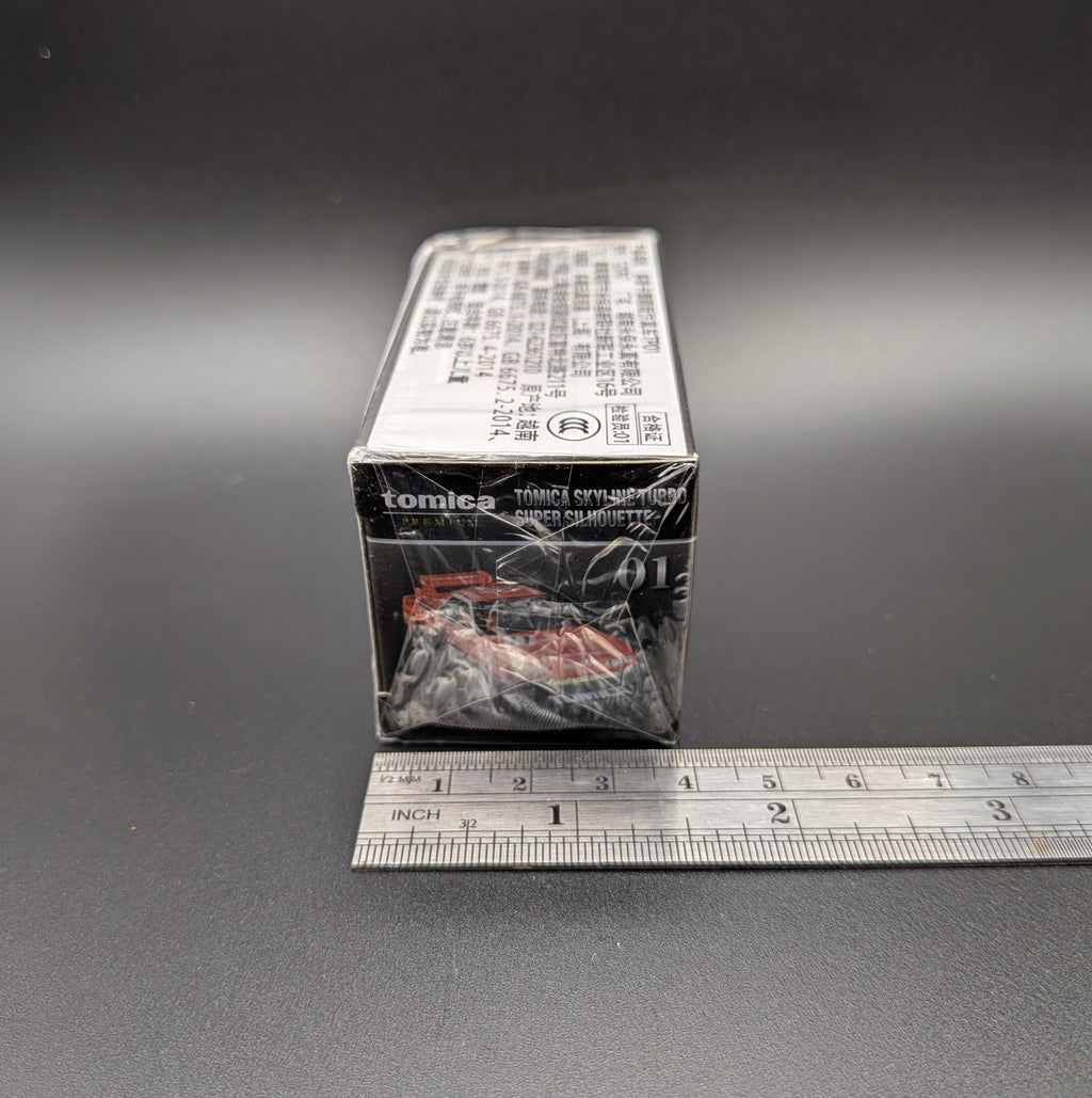 Tomica Premium model car of a Nissan Skyline Turbo Super Silhouette #01 in red and black with Tomica livery. The item is sitting side on  with a metal ruler beside the box to show the width (4cm) and sits on a grey background.