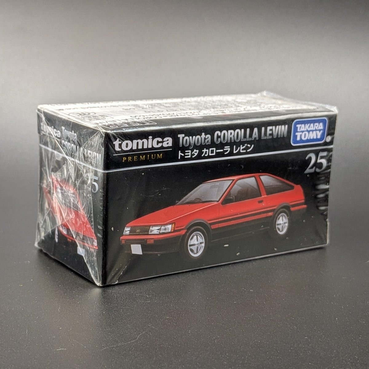A boxed Tomica Premium Takara Tomy Toyota Corolla Levin model car, number 25, in its original shrink-wrapped packaging on a dark gray background.