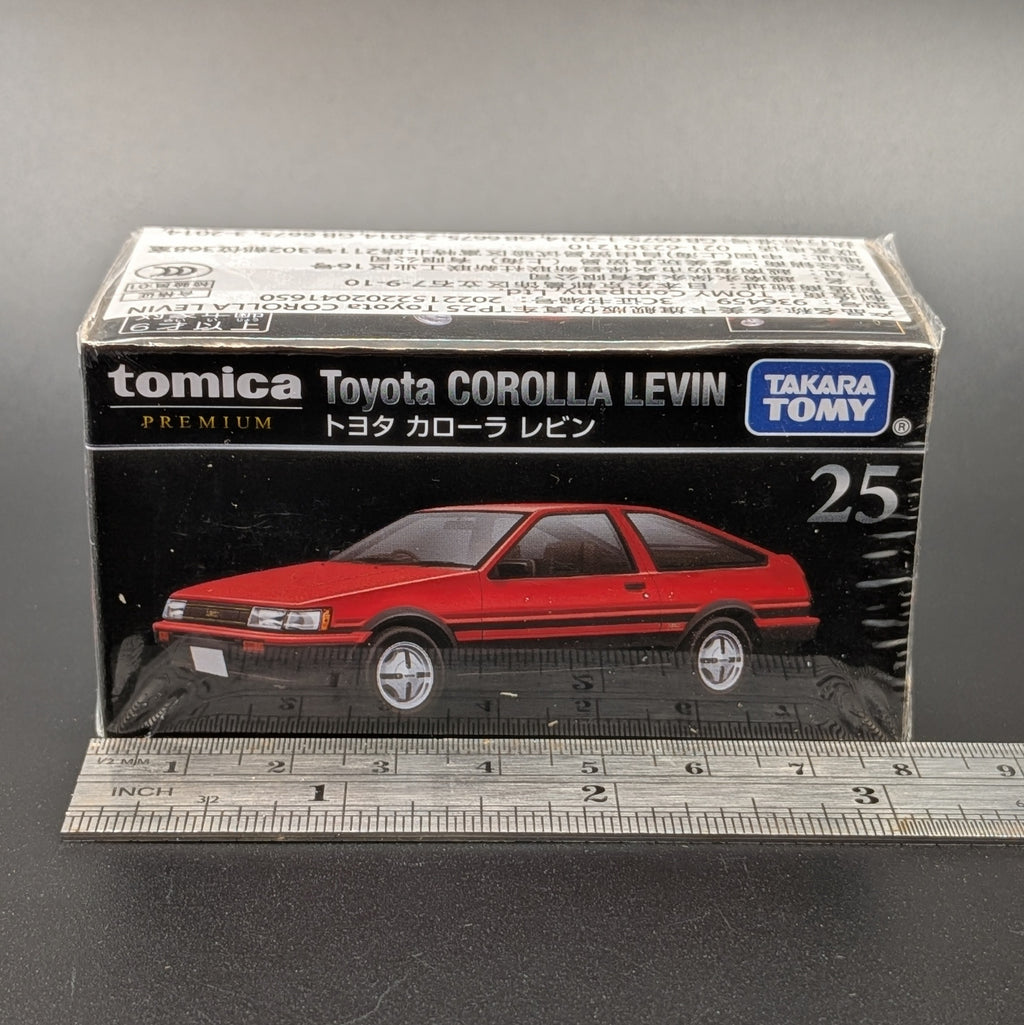 A boxed Tomica Premium toy car model, specifically the Toyota Corolla Levin number 25, shown in its original retail packaging with a metal ruler at the bottom for scale against a dark gray background.