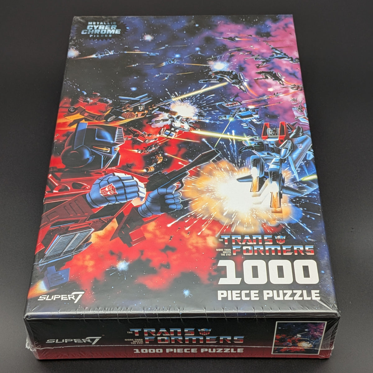 A 1000-piece jigsaw puzzle box featuring a colorful space battle scene with Transformers and other robot characters. The box is branded with 'Transformers' and 'Super7' and is photographed on a dark surface.