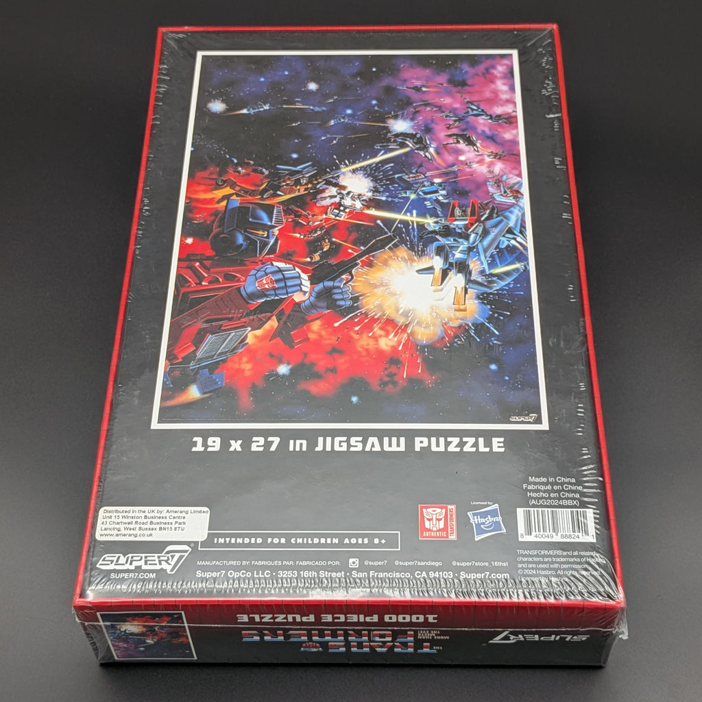 Transformers jigsaw puzzle box by Super7, featuring a puzzle with a space battle scene of red and blue robots in a starry galaxy. The box is sealed in plastic wrap and photographed on a dark background.