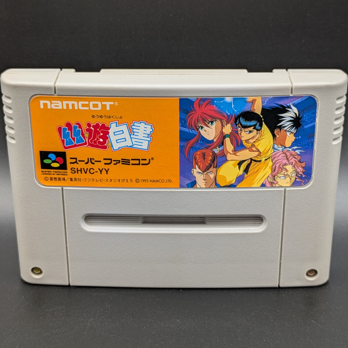 A close up of Yu Yu Hakusho video game cartridge for Nintendo's Super Famicom (SFC) Entertainment System, shown standing up and facing forwards on a dark grey background.