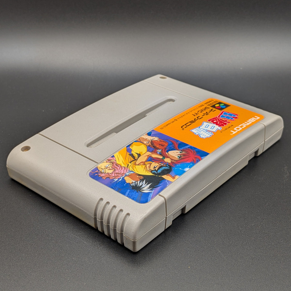 Yu Yu Hakusho video game cartridge for Nintendo's Super Famicom (SFC) Entertainment System, shown laying on its back with the label facing upwards. Showing the right hand side and top edge. It is displayed on a dark grey background.