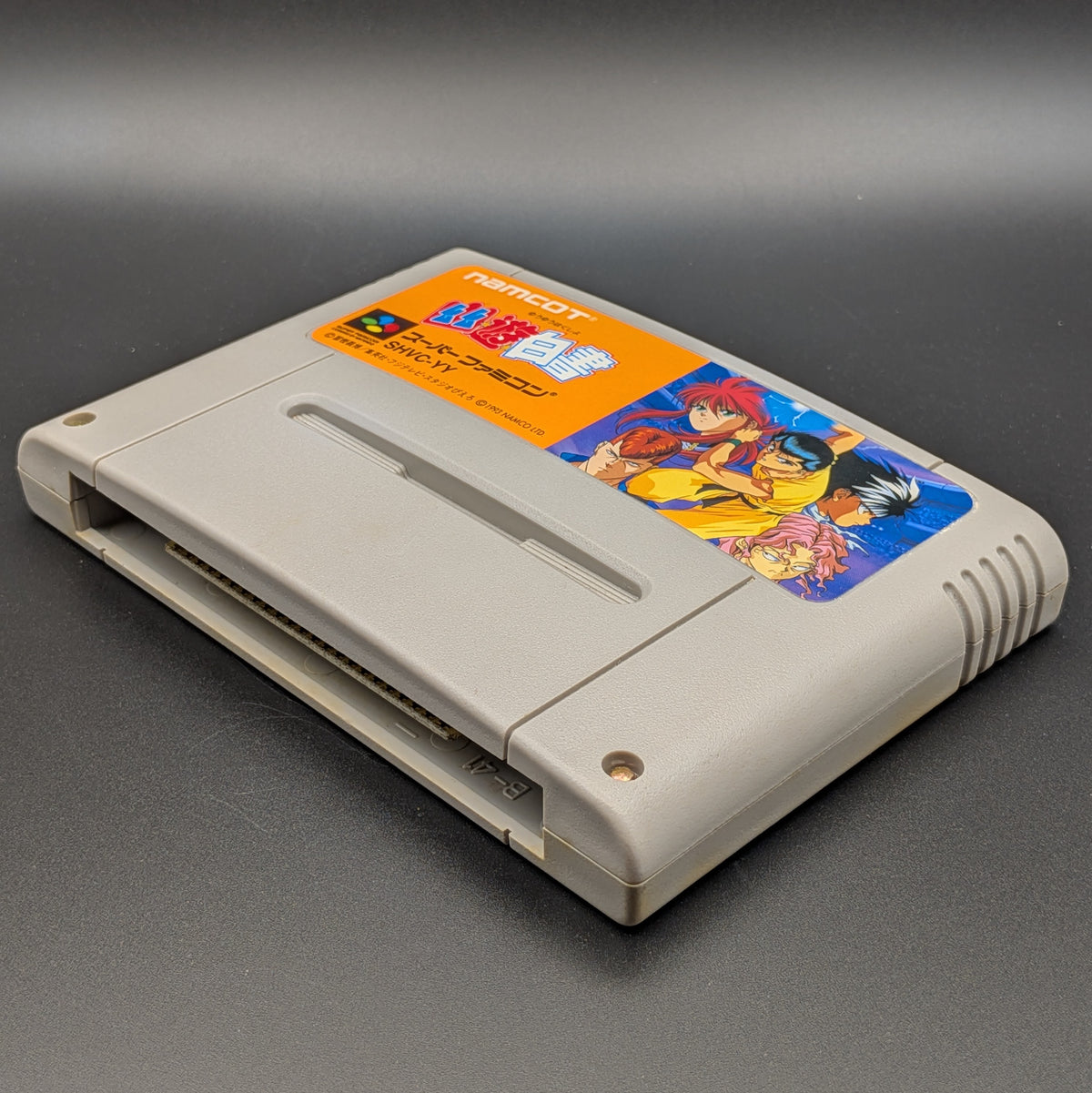 Yu Yu Hakusho video game cartridge for Nintendo's Super Famicom (SFC) Entertainment System, shown laying on its back with the label facing upwards. Showing the right hand side and bottom slot. It is displayed on a dark grey background.