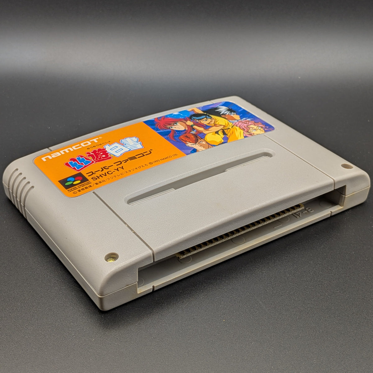 Yu Yu Hakusho video game cartridge for Nintendo's Super Famicom (SFC) Entertainment System, shown laying on its back with the label facing upwards. Showing the left hand side and bottom slot. It is displayed on a dark grey background.