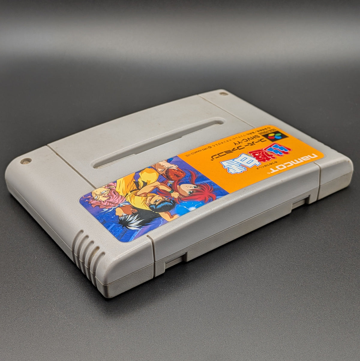 Yu Yu Hakusho video game cartridge for Nintendo's Super Famicom (SFC) Entertainment System, shown laying on its back with the label facing upwards. Showing the right hand side and top edge. It is displayed on a dark grey background.