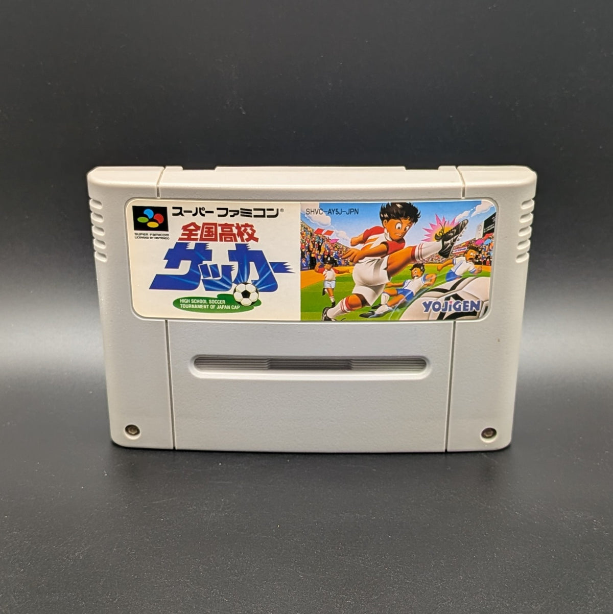Zenkoku Kōkō Soccer video game cartridge for Nintendo's Super Famicom (SFC) Entertainment System, shown standing up and facing forwards on a dark grey background.