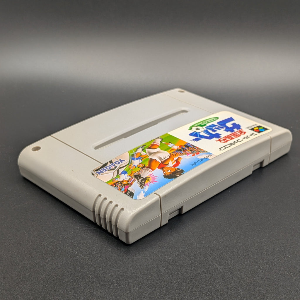 Zenkoku Kōkō Soccer video game cartridge for Nintendo's Super Famicom (SFC) Entertainment System, shown laying on its back with the label facing upwards. Showing the right hand side and top edge. It sits on a dark grey background.