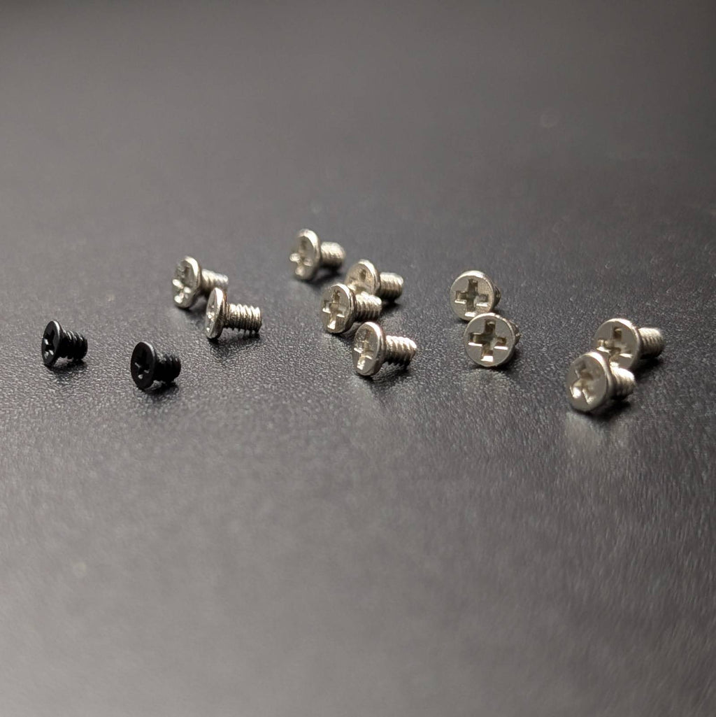 A set of small screws, including two black screws and several silver screws, arranged on a dark gray textured surface.