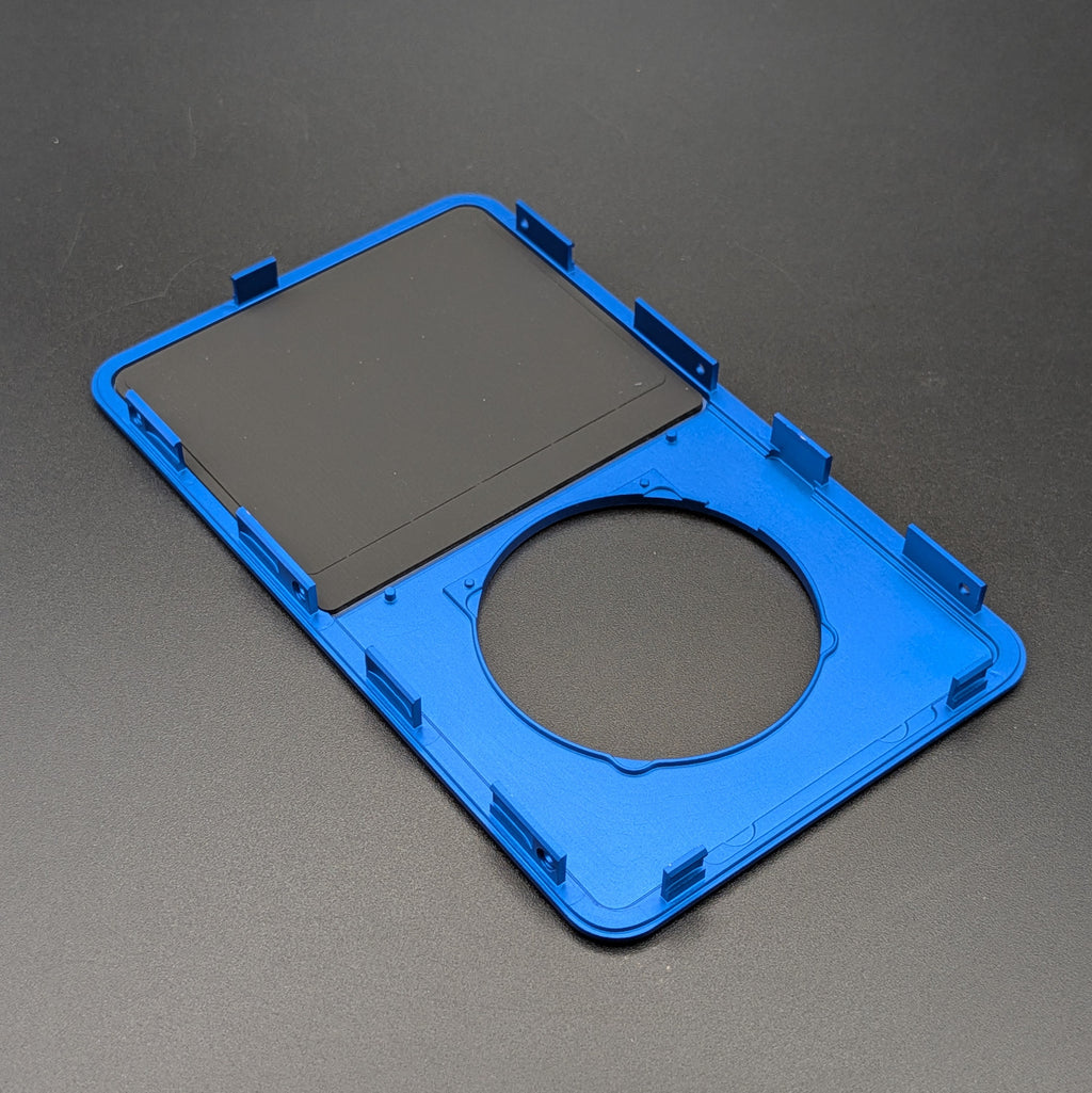 A blue replacement frame or bezel with a circular cutout and a rectangular black insert, photographed on a dark gray textured background.